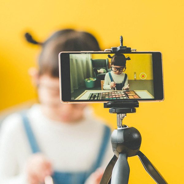 Image of Asian little cute girl wear eye wear play making a makeup with recording making video blogger camera for her blog at home. Vlogging concept.